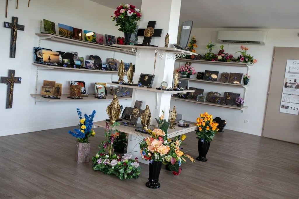 Boutique d'articles funéraires avec plaques commémoratives, statues de la Vierge Marie et compositions florales de deuil